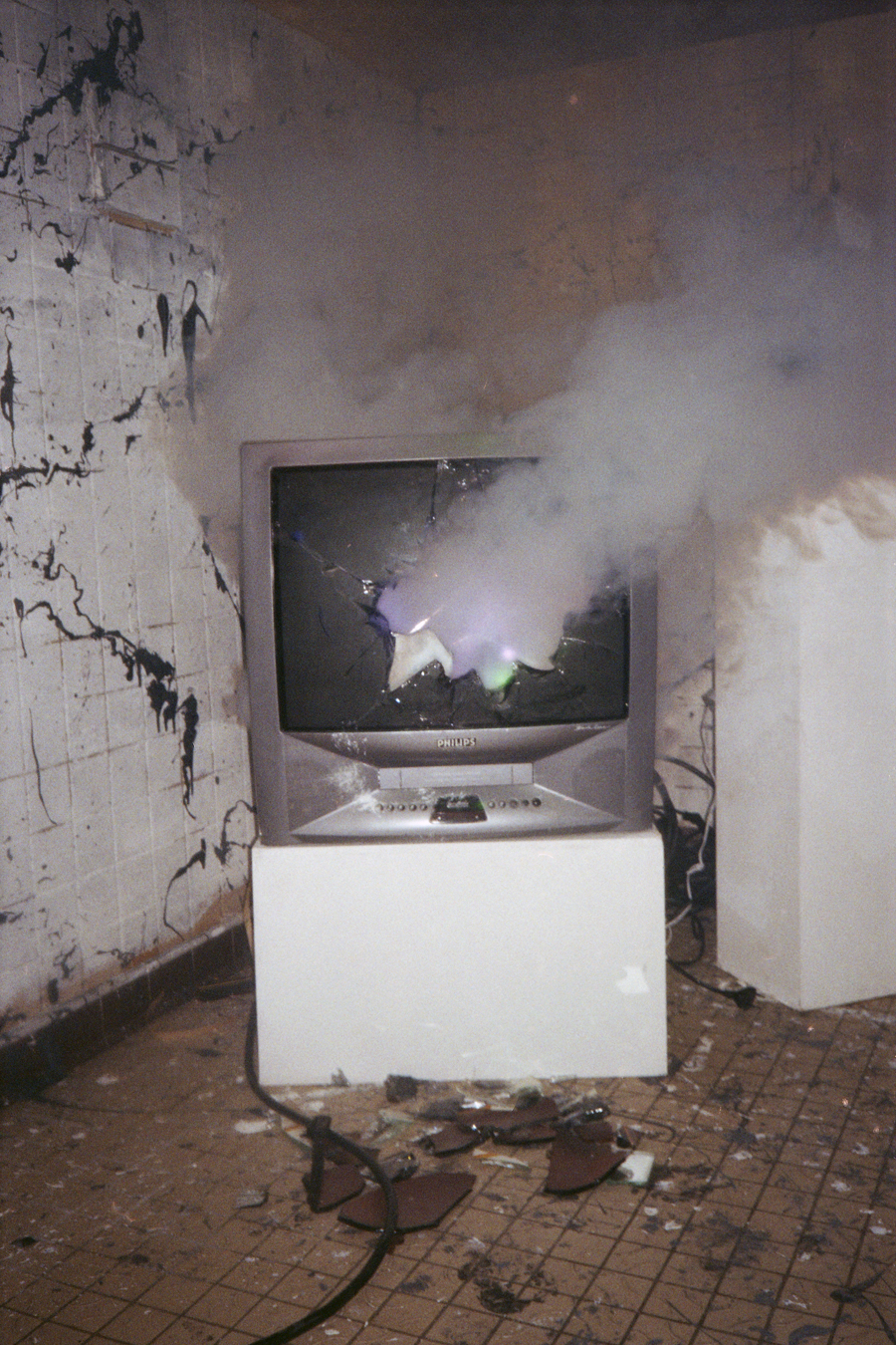 Photographie en argentique couleur d'une vieille télévision cathodique cassée où se propage de la fumée au centre.